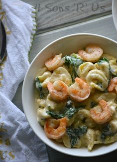 pasta with shrimp and spinach in a white bowl next to a fork on a table