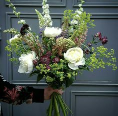 a person holding a bouquet of flowers in front of a gray door with green foliage