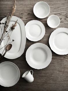 white dishes and cups are arranged on a wooden table with dried flowers in vases