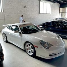 a man standing on top of a white sports car in a garage next to other cars