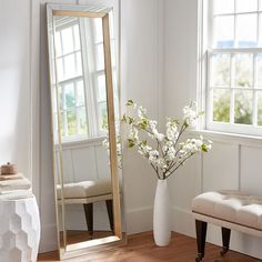 a large mirror sitting next to a white vase filled with flowers on top of a hard wood floor