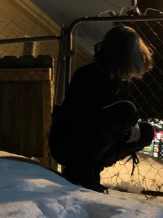 a person sitting in the snow near a fence