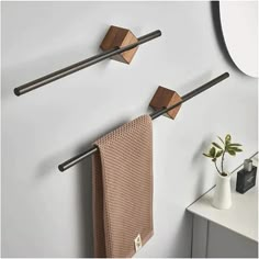 two metal and wood towel racks on the wall next to a white vase with a plant in it