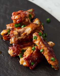 chicken wings with sauce and green onions on a black plate