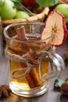 an apple cider with cinnamon sticks in it and some apples around the glass cup