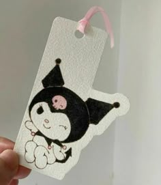 a person holding up a white tag with a black and pink cartoon penguin on it