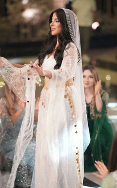 a woman in a white dress and veil standing next to other women wearing green dresses