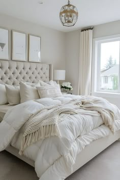 a white bed sitting next to a window in a bedroom under a chandelier