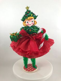 a doll is dressed in red and green with a christmas tree on it's head