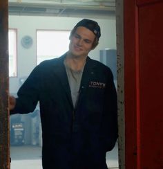 a man in a black jacket is standing by a red door