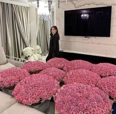 a woman standing next to a bunch of pink flowers in front of a flat screen tv