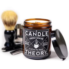 a candle next to a shaving brush on a white surface with other items around it