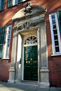 a green door is in front of a brick building with white trimmings and windows