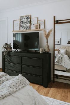 a bedroom with a dresser, mirror and television on it's stand in front of a bed