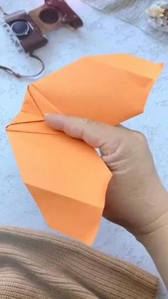 someone holding an orange paper airplane in their hand