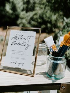 a sign that says abstract painting next to some paintbrushes in a glass jar