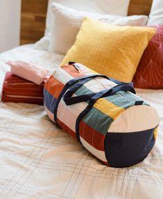 a bag sitting on top of a bed next to pillows and pillow cases with different colors