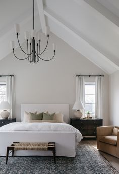 a large white bed sitting under a chandelier in a bedroom next to two chairs