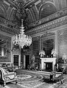 an old black and white photo of a living room with chandelier, couches, chairs and fireplace