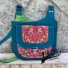 a purse with a tiger design on the front and shoulder strap, sitting against a stone wall