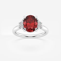 a ring with a red stone and two white diamonds on the band, set in 18k white gold