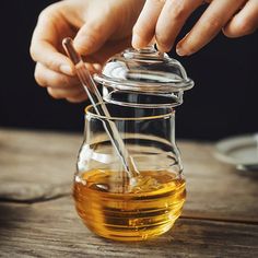 a person is pouring oil into a glass jar with a spoon on a wooden table