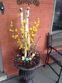 a vase filled with yellow flowers next to a chair and brick wall in front of a building