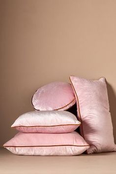 pink pillows stacked on top of each other in front of a beige wall and tan background