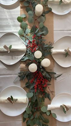 the table is set with white plates and greenery