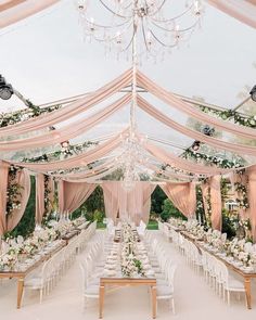 an outdoor wedding reception setup with chandeliers and white linen draping on the ceiling