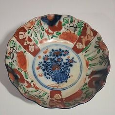 a decorative bowl with flowers and leaves painted on the side, sitting on a white surface