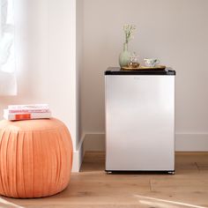 a small white refrigerator sitting next to a table with a vase on top of it