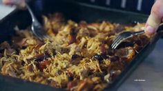 a person holding a fork and spoon in a casserole dish full of food