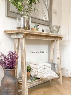 a wooden table with flowers and towels on it in front of a mirror, next to a potted plant