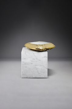 a white and gold object sitting on top of a marble block in front of a gray background