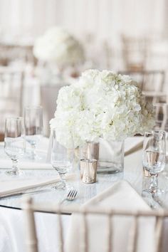 a table with white flowers and silverware is set for a formal dinner or reception