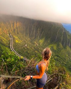 a woman standing on top of a mountain next to a lush green hillside