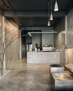 the interior of a coffee shop with concrete walls and flooring is lit by pendant lights