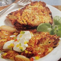 a white plate topped with hash browns covered in sour cream and veggies next to a fork