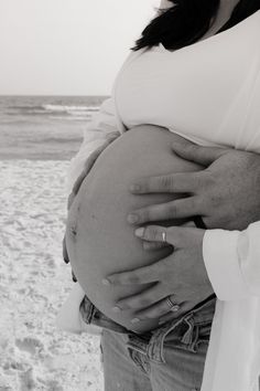 a pregnant woman holding her husband's belly on the beach