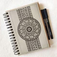 a spiral notebook with an intricate design and two black pens