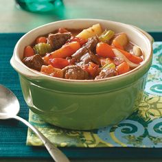 a green bowl filled with meat and vegetables on top of a blue place mat next to a spoon