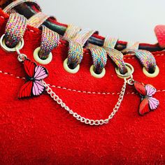 a pair of red shoes with butterfly charms on the laces and chains attached to them