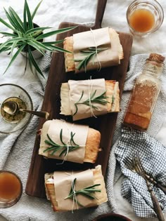 four wrapped sandwiches on a wooden tray with rosemary sprigs tied around the edges