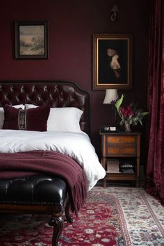 a bedroom with red walls, white bedding and an antique style leather headboard