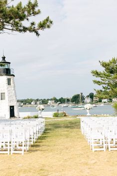 an outdoor ceremony setup with white chairs and a light house in the background at a wedding