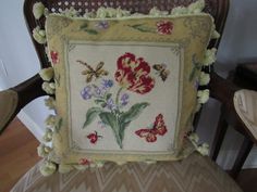 a cushion with flowers and butterflies on it sitting on a chair in front of a wall