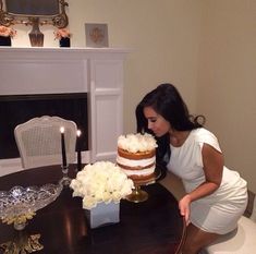 a woman is cutting into a cake on a table in front of a fire place