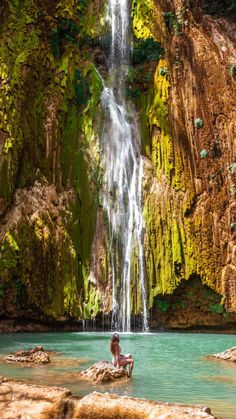 a person sitting in front of a waterfall with green moss growing on the rocks and water