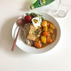 a white plate topped with rice, meat and veggies next to a bottle of beer